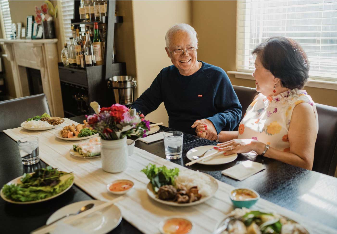 An elderly couple laughing and talking over a meal.